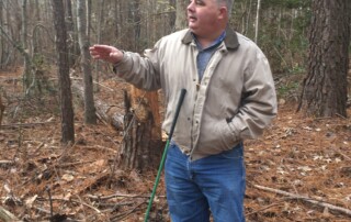 A man talking and pointing off to the side. He is in a forest