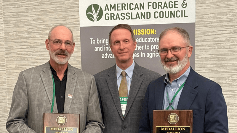 Three men holding awards in front of a banner that reads American Forage and Grasslands Council