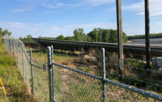 A fence cuts diagonally across the photo. On the far side of the fence are two electrical poles and a field of solar panels