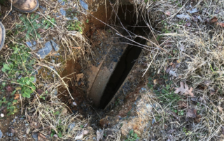 Birds eye view of a rectangular small hole in the ground. This hole shows a large pipe that is not fully connected