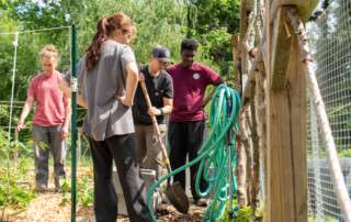 WNCStrong Youth Service Corps participants Sofia, Ali, and Phoenix stand with Bountiful Cities garden manager Micah Nielsen in an Asheville community garden.